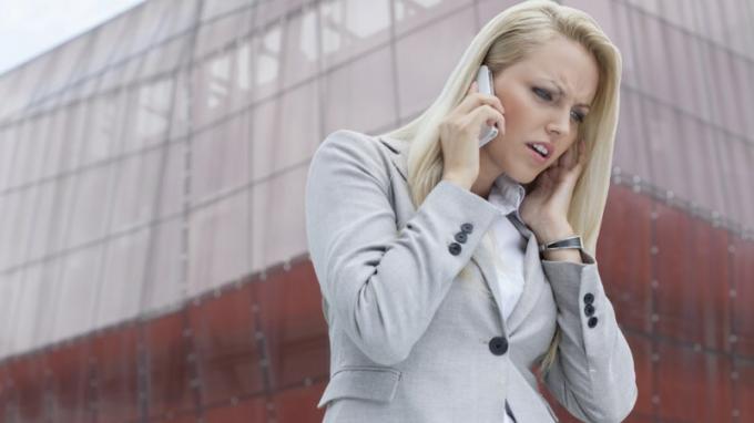 Sieviete ar ADHD, klausoties kādam mobilajā telefonā un sadusmojoties augstās ēkas priekšā