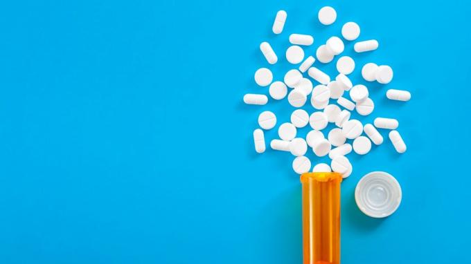 Medicīna, opioīdu pretsāpju un recepšu zāļu koncepcija ar skatu uz apelsīnu recepšu pudeli oksikodona un hidrokodona tabletes, kas izlijušas uz zila fona ar kopiju