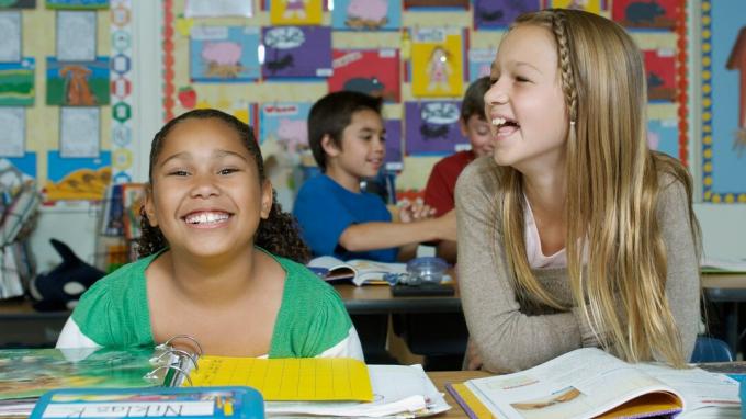 Divas skolnieces ar ADHD sēž pie galda un smejas